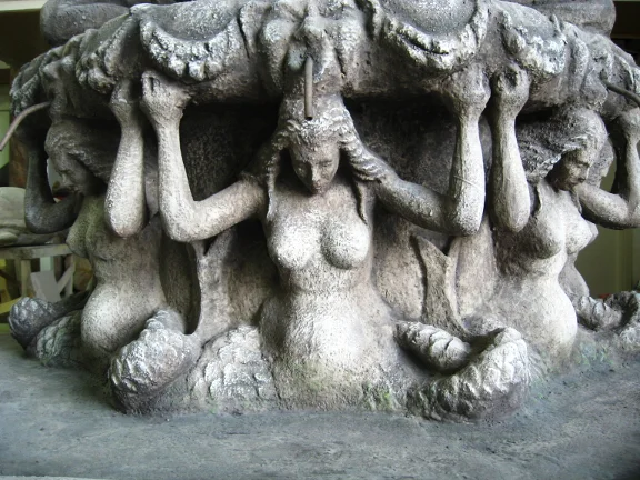 Close-up detail of the Fountain of the Four Moors: the four female caryatids seen in the foreground, arms raised holding the pedestal above, finish in weathered stone grey with green moss accents sculpted in, modulated drapery