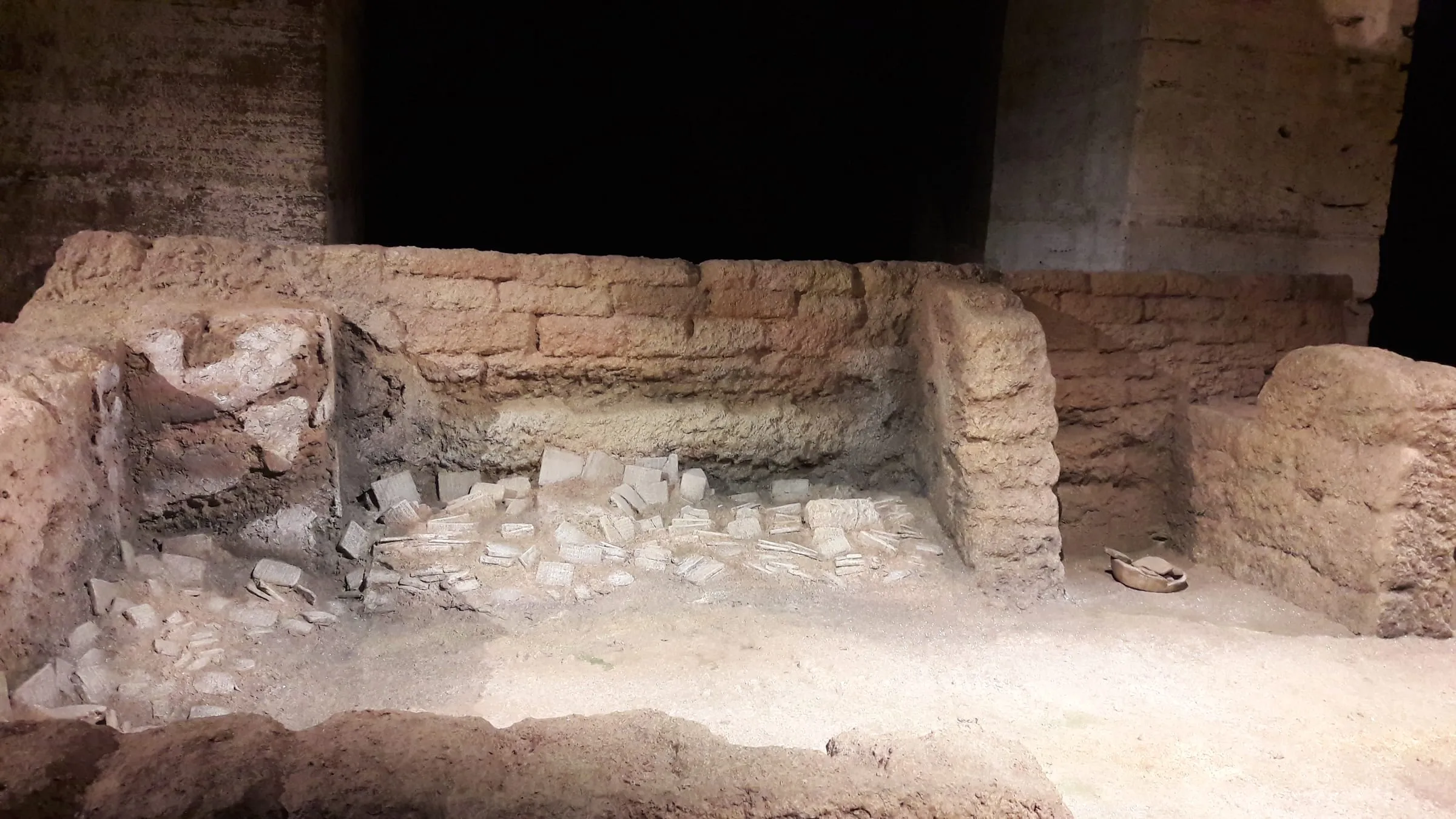 La Sala dell'Archivio di Ebla installata al Colosseo: muratura in crudo color sabbia, tavolette cuneiformi cadute sul pavimento, illuminazione laterale