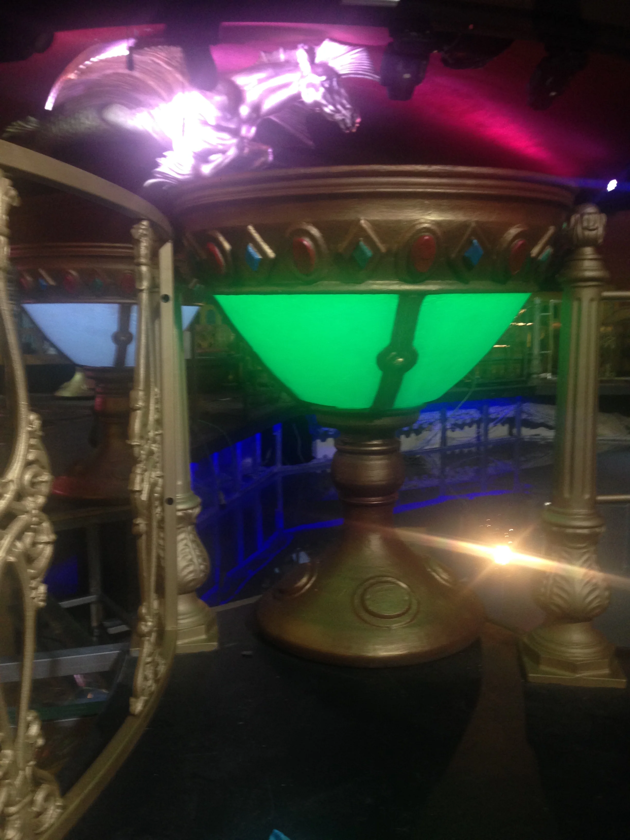 Two luminous goblets in the foreground lit in different tones — one neon blue, one cool white — view of the chromatic effect in the underground galleries of the venue