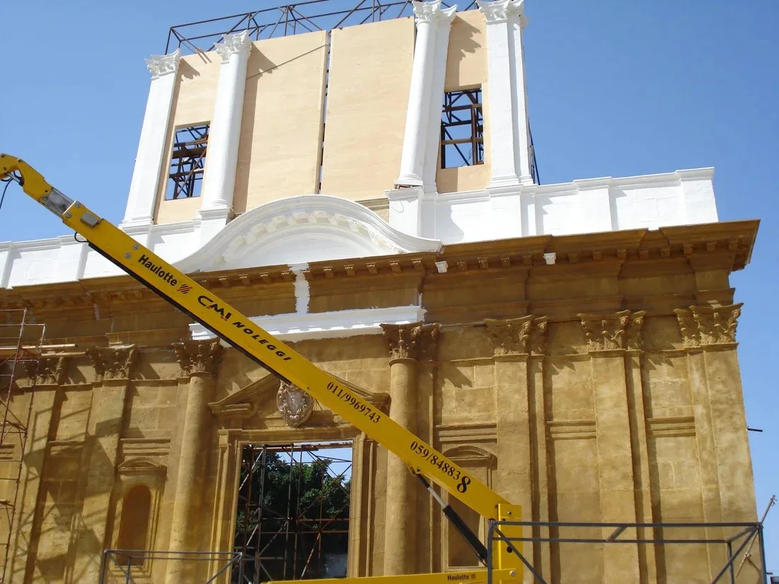 A Sicilian Baroque church rebuilt in Tunis, mustard-yellow, still under construction with a service crane