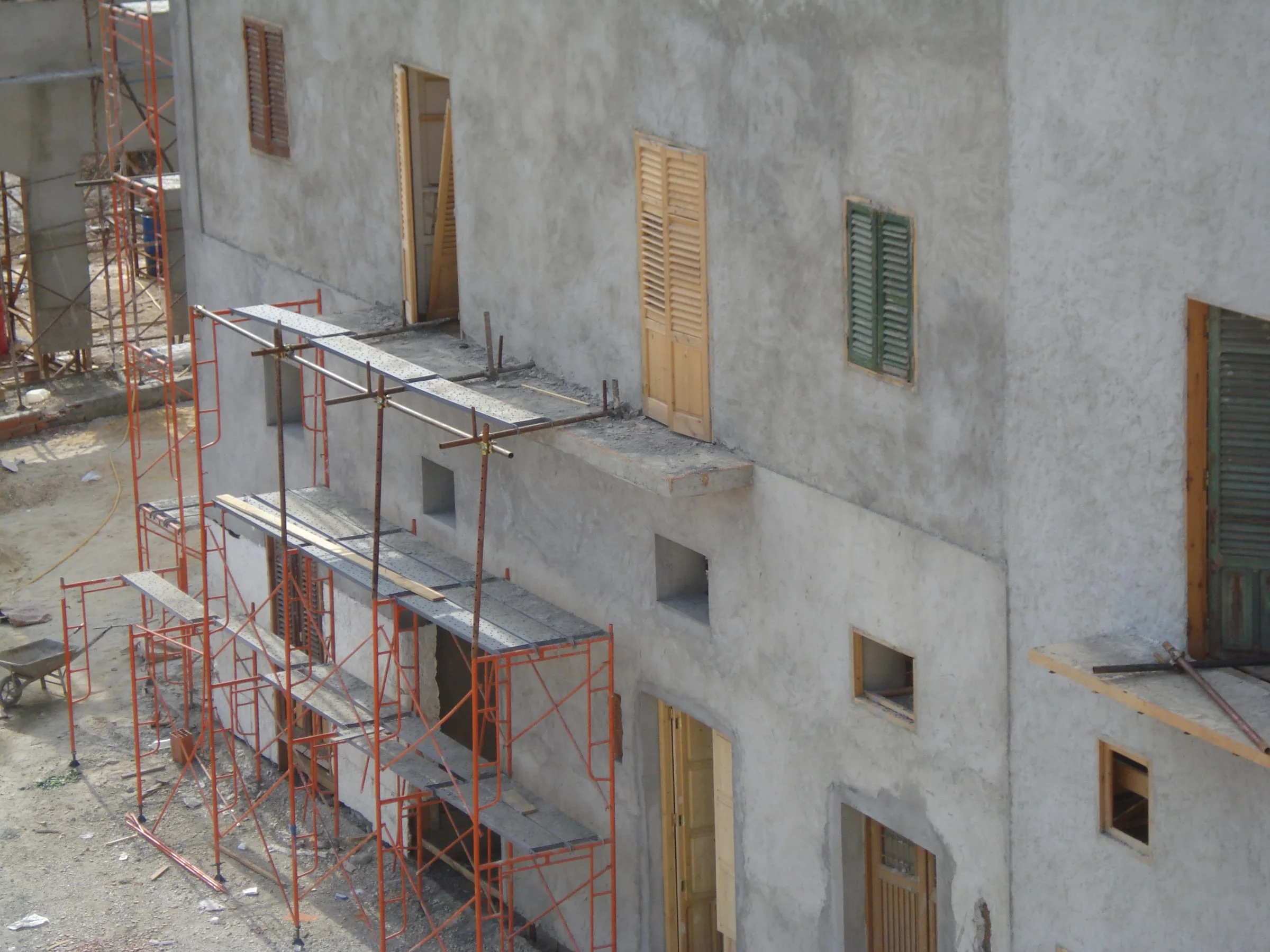 Facades of a working-class palazzo in faux Sicilian stone, scaffolding still active after the grey rendering