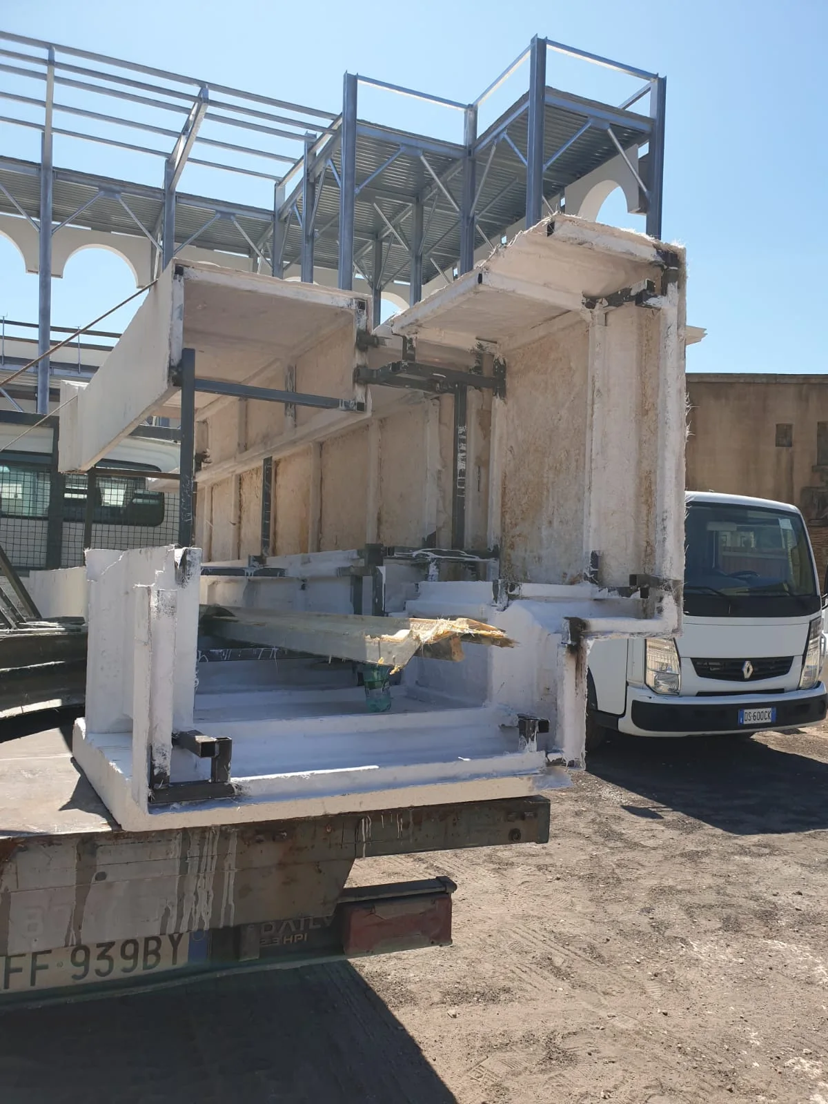 Vista panoramica del cantiere della Basilica Giulia il 7 agosto 2019: tutto l'edificio si vede frontalmente, primo piano d'archi in pietra finta bianca completato, secondo piano in struttura metallica scheletro tubolare, in primo piano basolato della pavimentazione, sullo sfondo case residenziali