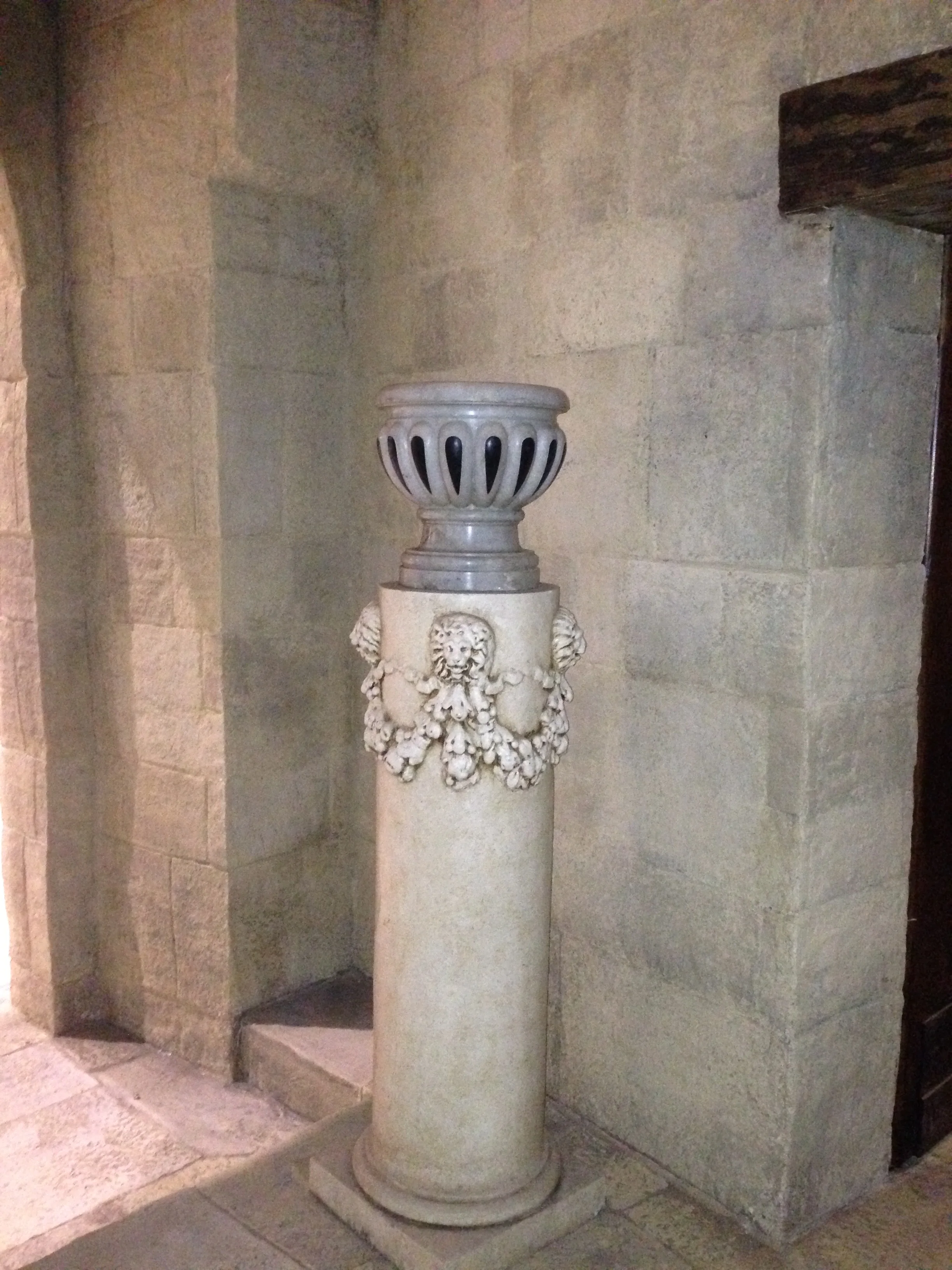 Colonna in finta pietra marmorea per il set di Ben Hur: festone di foglie scolpite e due teste leonine ai lati, capitello traforato a forma di bocciolo; il pezzo è posato in un nicchione del laboratorio con muratura in finta pietra ai lati