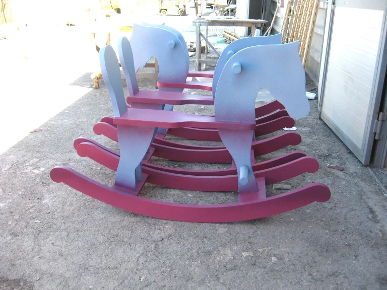 Pair of oversize rocking horses in the workshop yard: stylised horse in pale blue on magenta crescent-shaped rockers