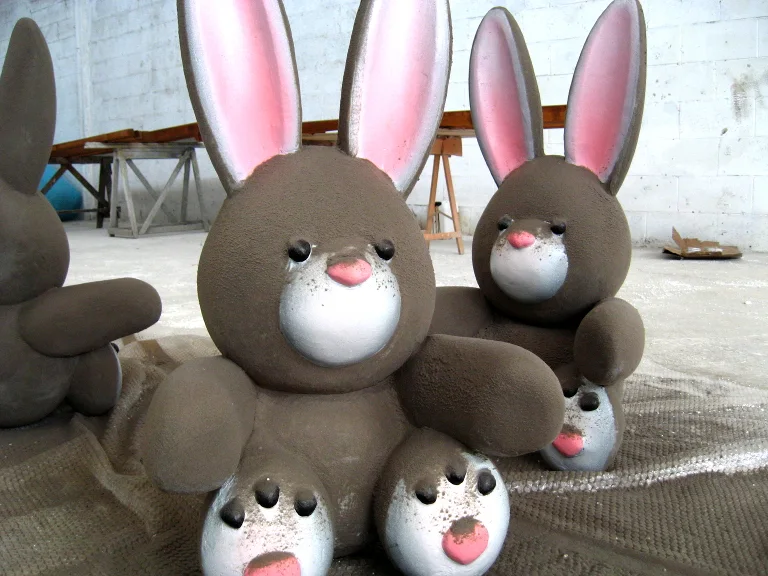 Family of bunnies sculpted in fibreglass, still raw: brown fur, tall ears with pink inside, pink nose, black eyes, two large adults and two smaller cubs, warehouse in the background