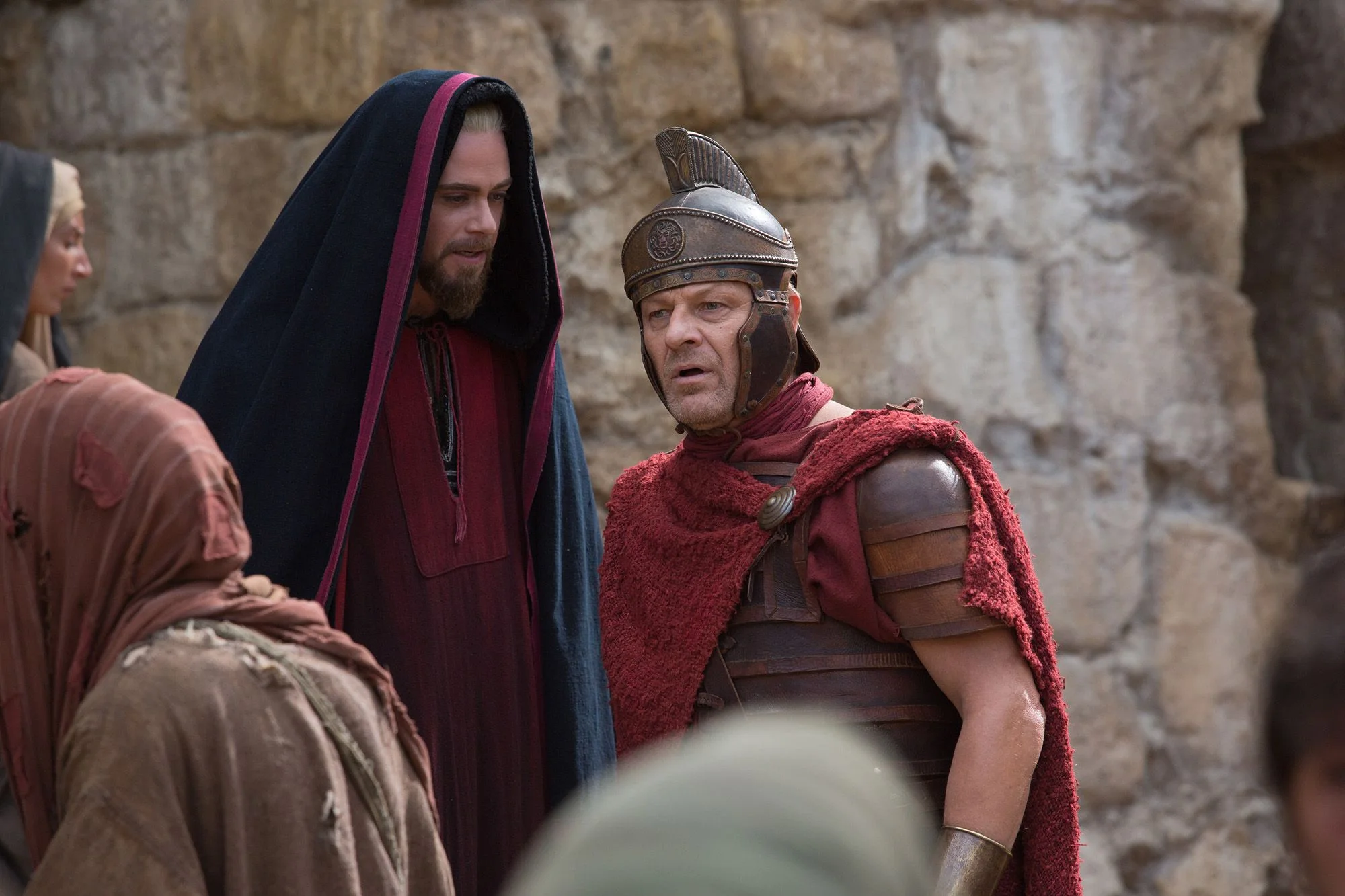 Sean Bean nei panni del centurione romano Severus, elmo di bronzo crestato, mantello rosso, accanto a un personaggio incappucciato. Muri di pietra antica sullo sfondo