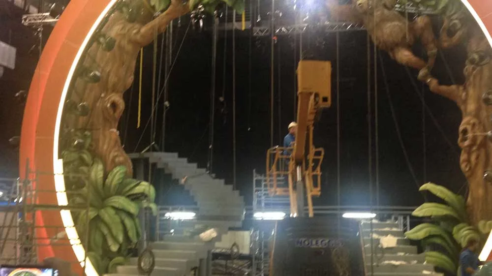 Interior view of the portal with a central cherry-picker for finishing work: orange portal ring closed around the scene, trunks and leaves on the sides, twin white staircase at the centre, black studio backdrop behind