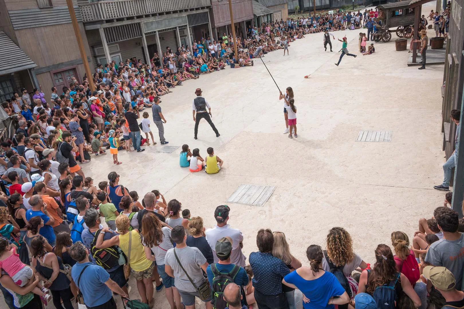 'Motori, ciak... azione!' stunt show in the Far West square, two actors at the centre, large audience in a circle around, wooden buildings in the background