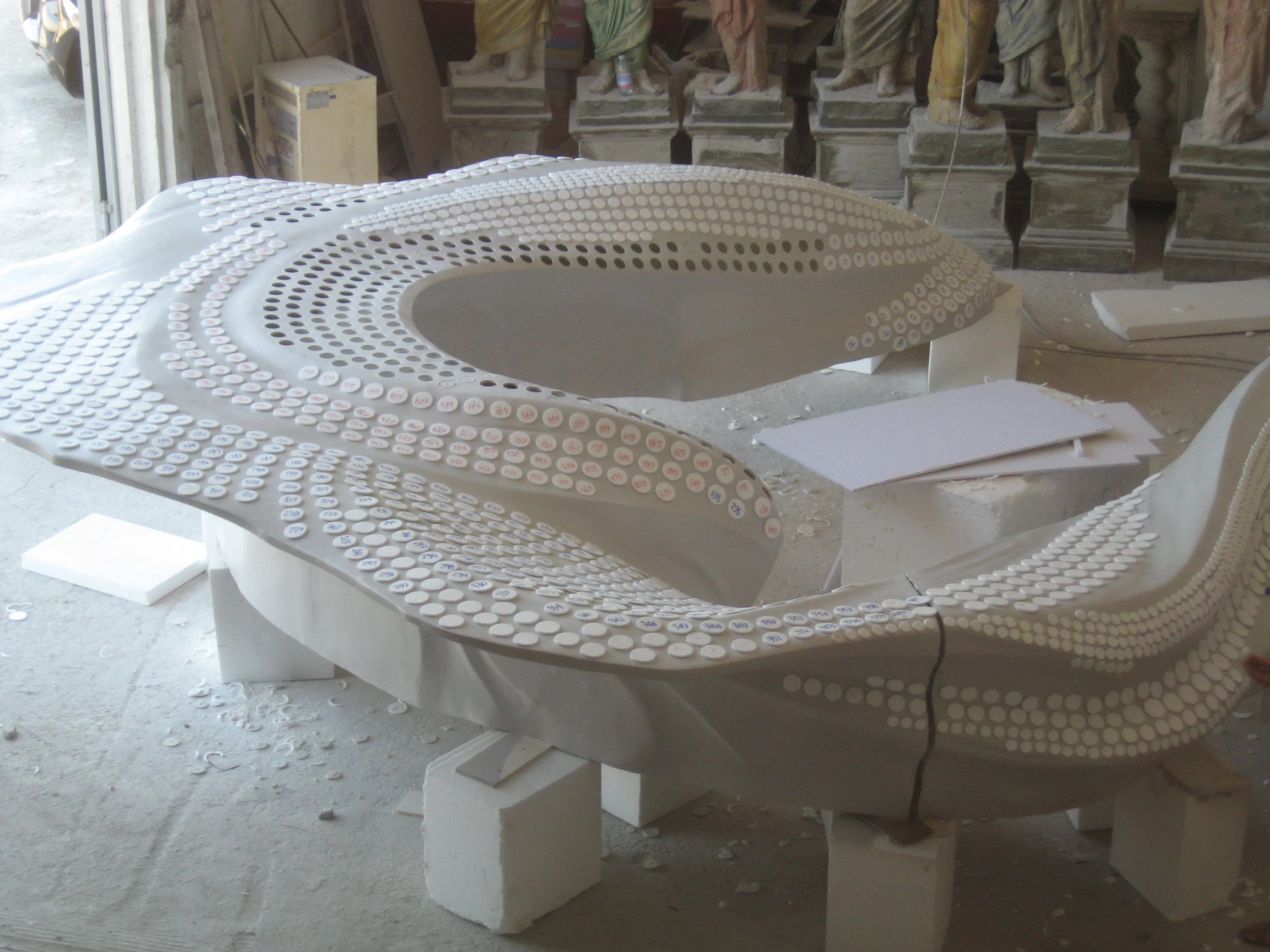 Detail of the desk seen from above in the workshop: sinuous white form with thousands of point-grid perforations arranged in concentric bands, each hole calibrated to host an addressable LED