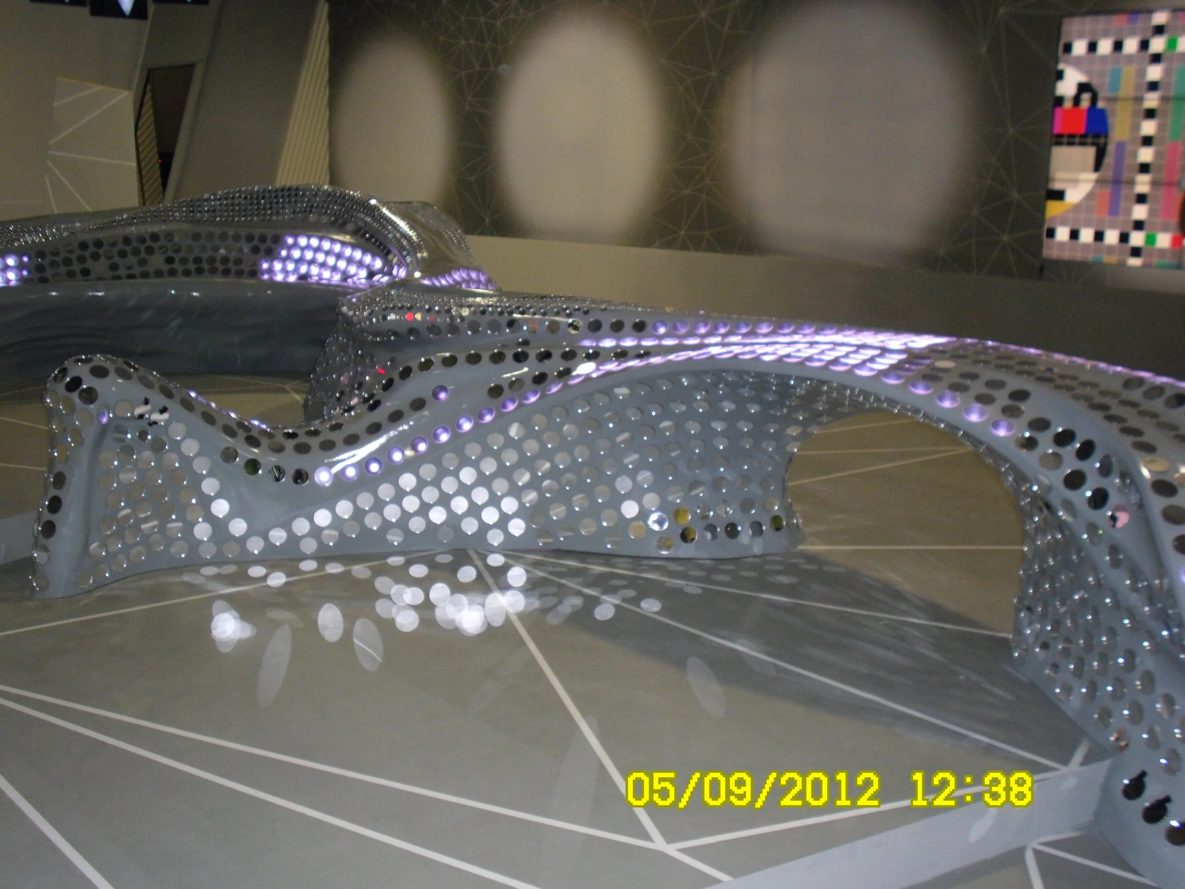 The desk installed at the Infront Studios in Milan during testing: surface still in grey primer, LEDs lit as purple points across the sinuous form, signal test monitors and technicians at work around it