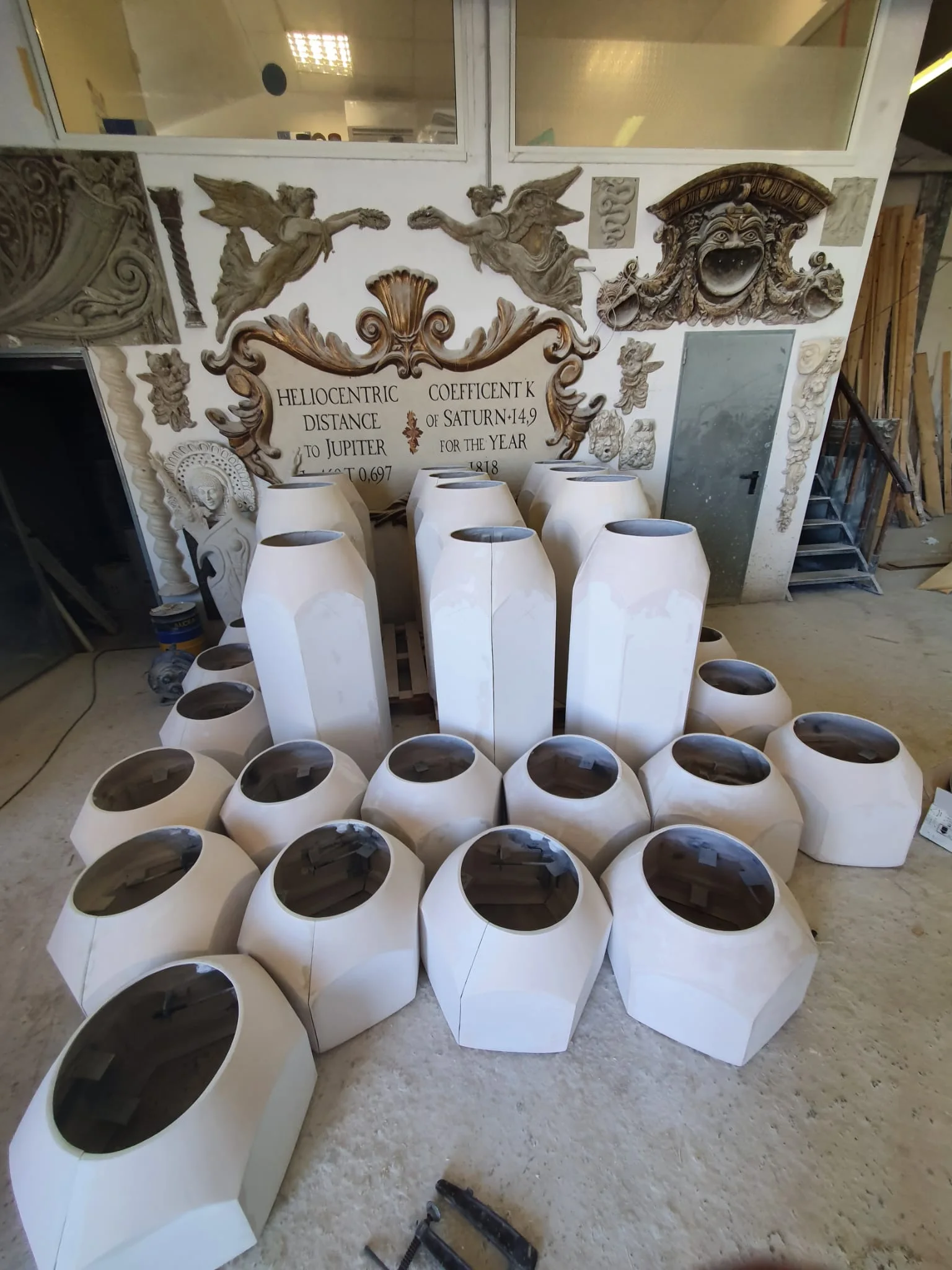 Vista laterale della casetta-officina in polistirolo: forma squadrata con tetto spiovente in lamiera ondulata grigia, una porta sulla parte frontale visibile, pareti in pannelli stratificati, panorami in lontananza del cantiere