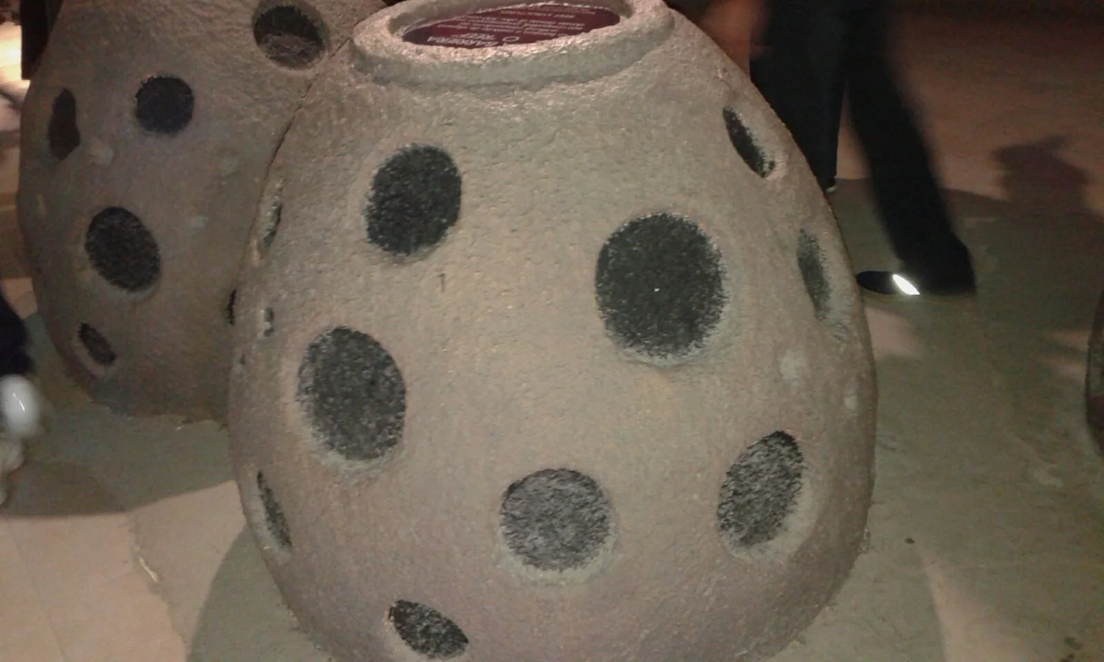 Reef Balls of the Oman Pavilion at Expo Milano 2015: two grey bell-shaped scenographic elements about a metre and a half tall, with round side holes mimicking openings for marine fauna, black labels on top for the captions of the Pro-Creator marine repopulation project
