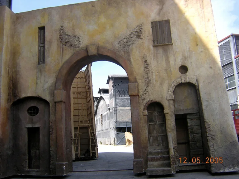 Portale ad arco e facciate dipinte del borgo toscano costruito a Papigno, con un'impalcatura tecnica visibile attraverso l'arco