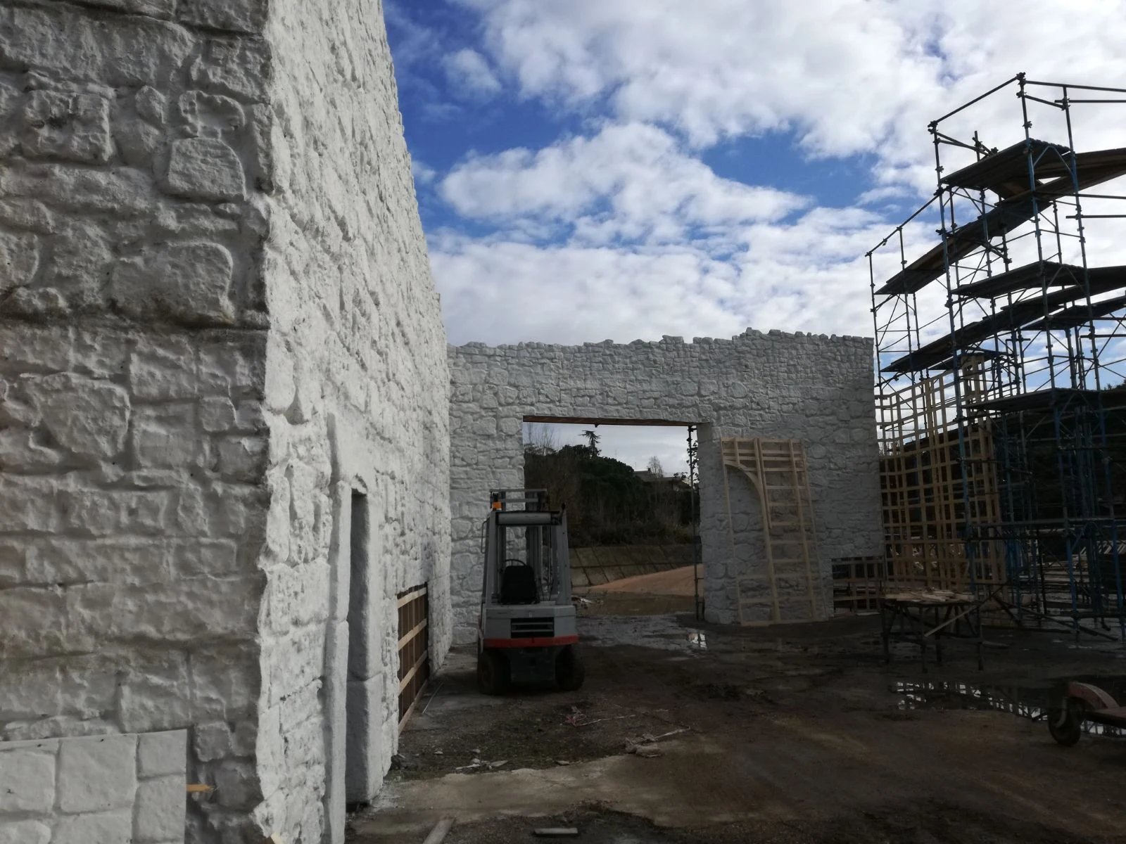 Vista del backlot esterno: pareti di pietra dell'abbazia, portale a tutto sesto in pietra bianca, muletto in primo piano davanti al portale, ponteggi sullo sfondo
