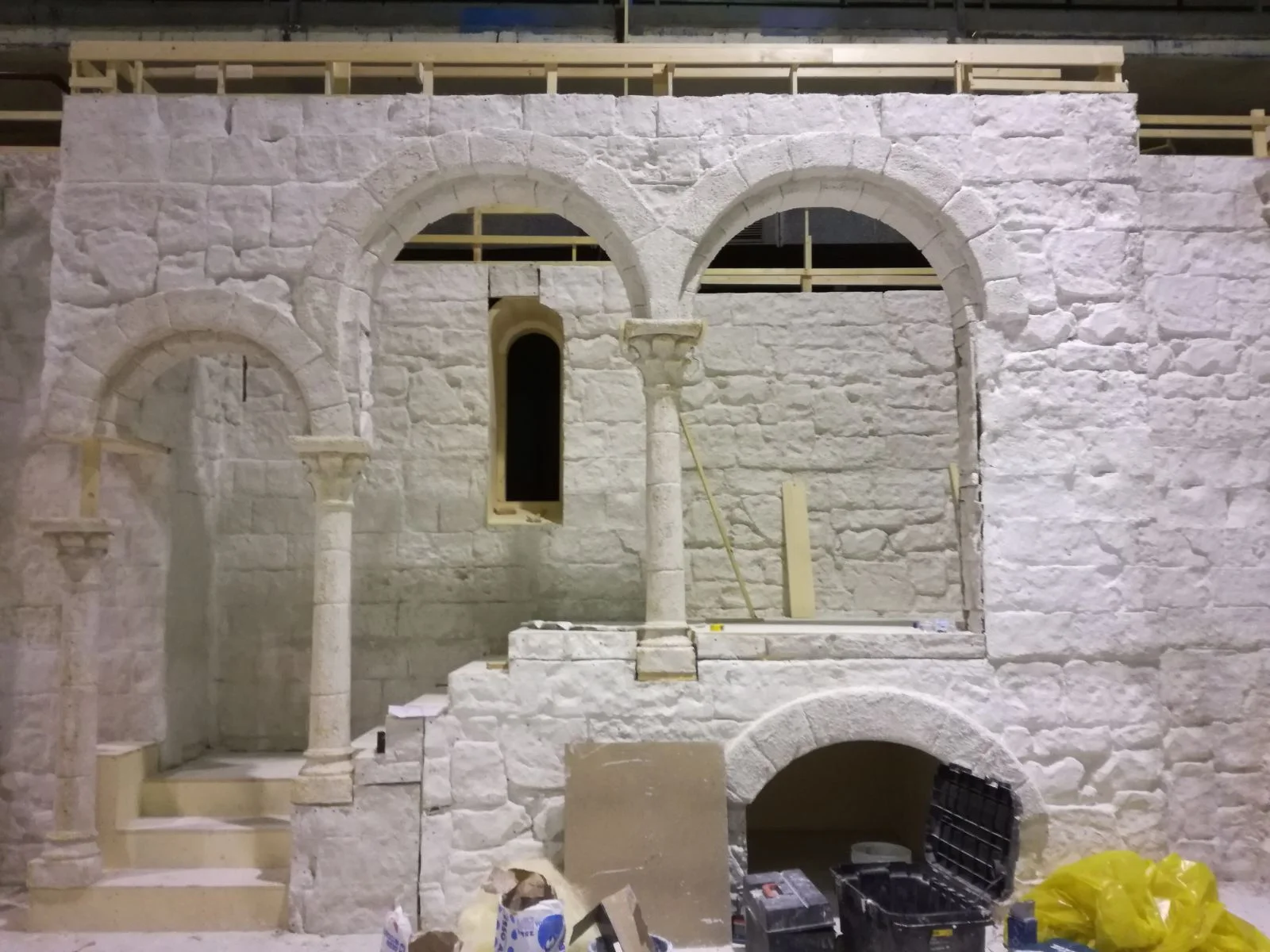 Trifora gotica con tre archi a tutto sesto e oculo centrale, colonnine in pietra finta scolpite, mura in pietra a vista. Vano interno dell'abbazia in lavorazione