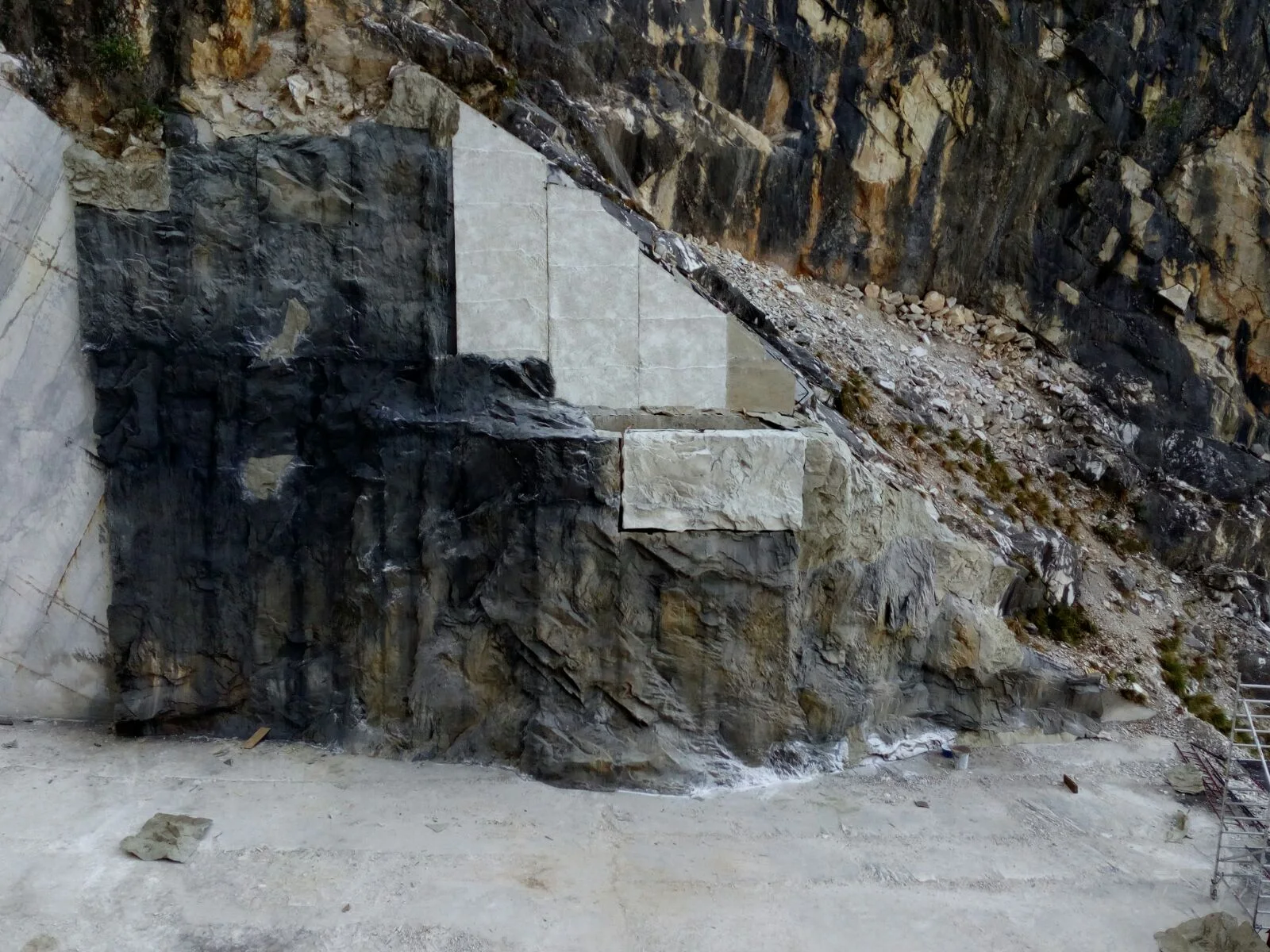 The completed scenographic intervention inside the Carrara quarry for Sin: the dark-grey quarry wall with white faux-marble triangular panels applied as cusps, the profile resembling a section of freshly cut marble, floor white with marble dust at the foot of the quarry