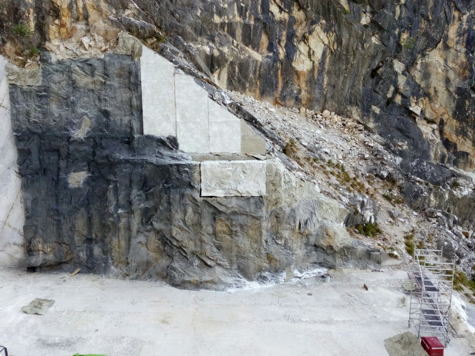 The scenographic intervention in its early phase: a white faux-marble triangular cusp applied onto the grey quarry wall, a scree of marble offcuts on the right, scaffolding lower right