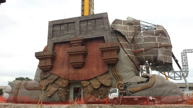Side view of the elephant being worked: 3/4 view with the entire structure visible, fountain at its feet, area buildings in the background