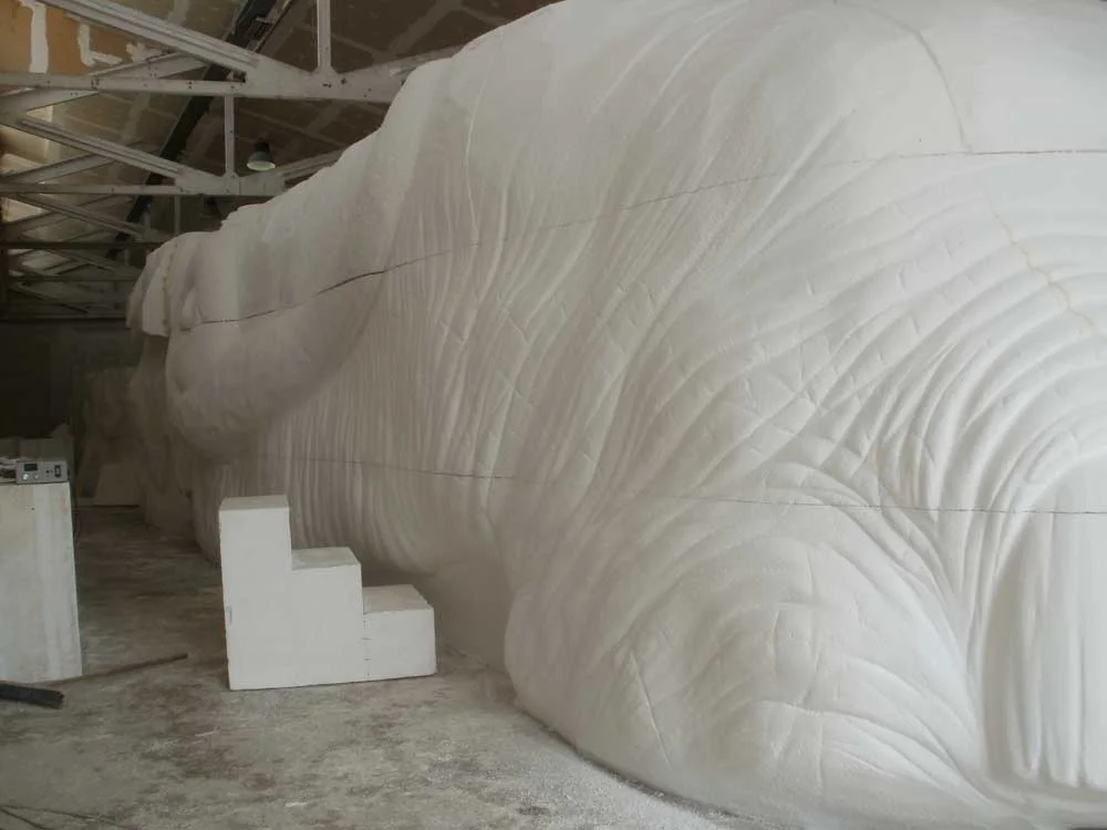 Large body section of the elephant in raw polystyrene, long lateral view, skin folds modelled to the millimetre, workshop shelves in the background