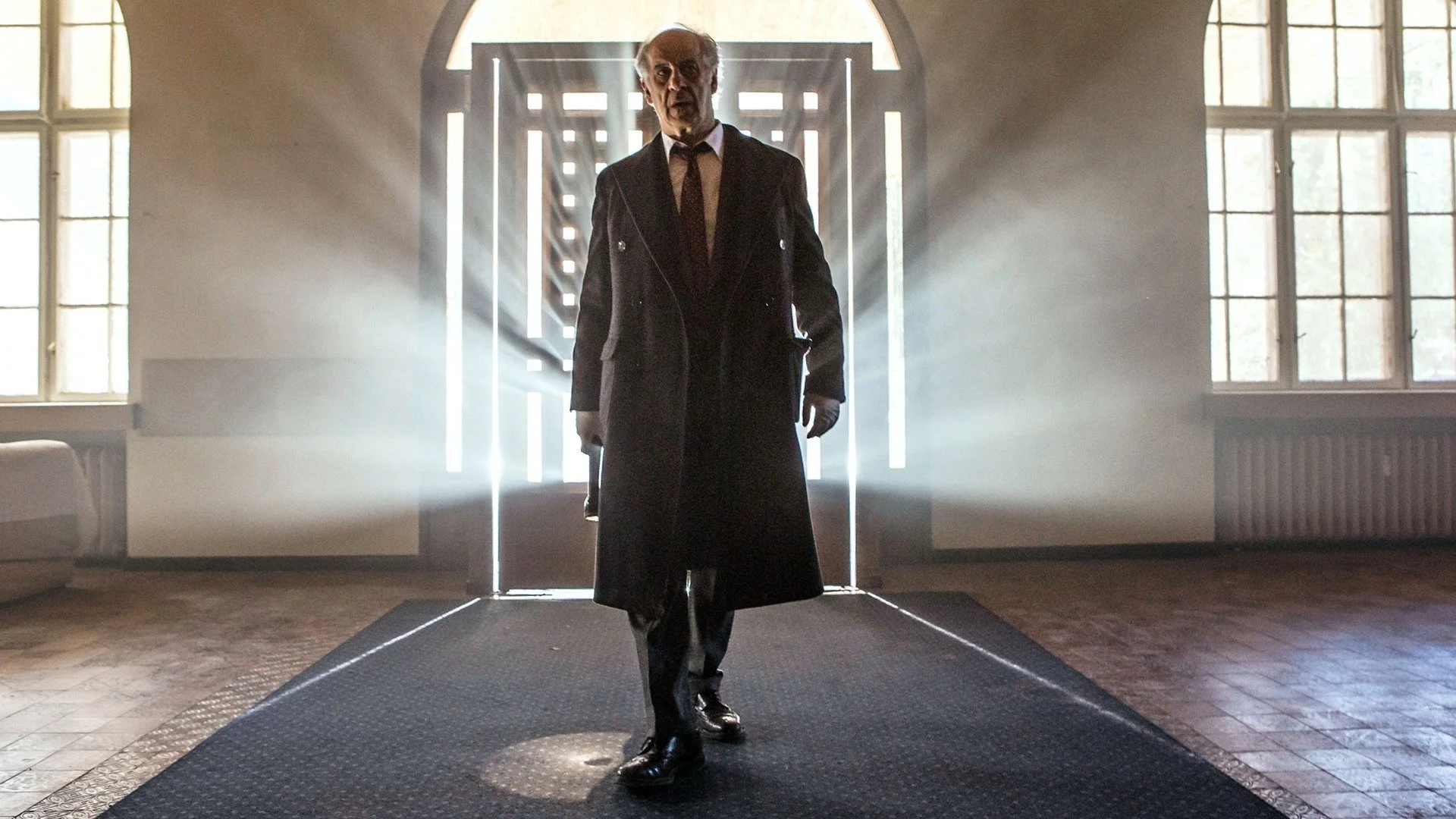 Toni Servillo as agent Vogel, standing at the centre of a room interrogated by a focused LED light beam.