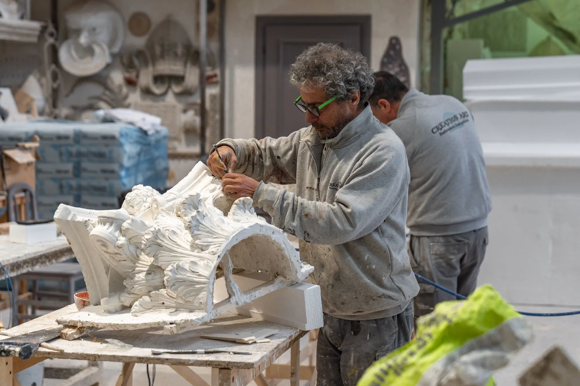 Un nostro operaio lavora a un capitello scenografico nei laboratori — vista dal piazzale, sotto la luce del capannone