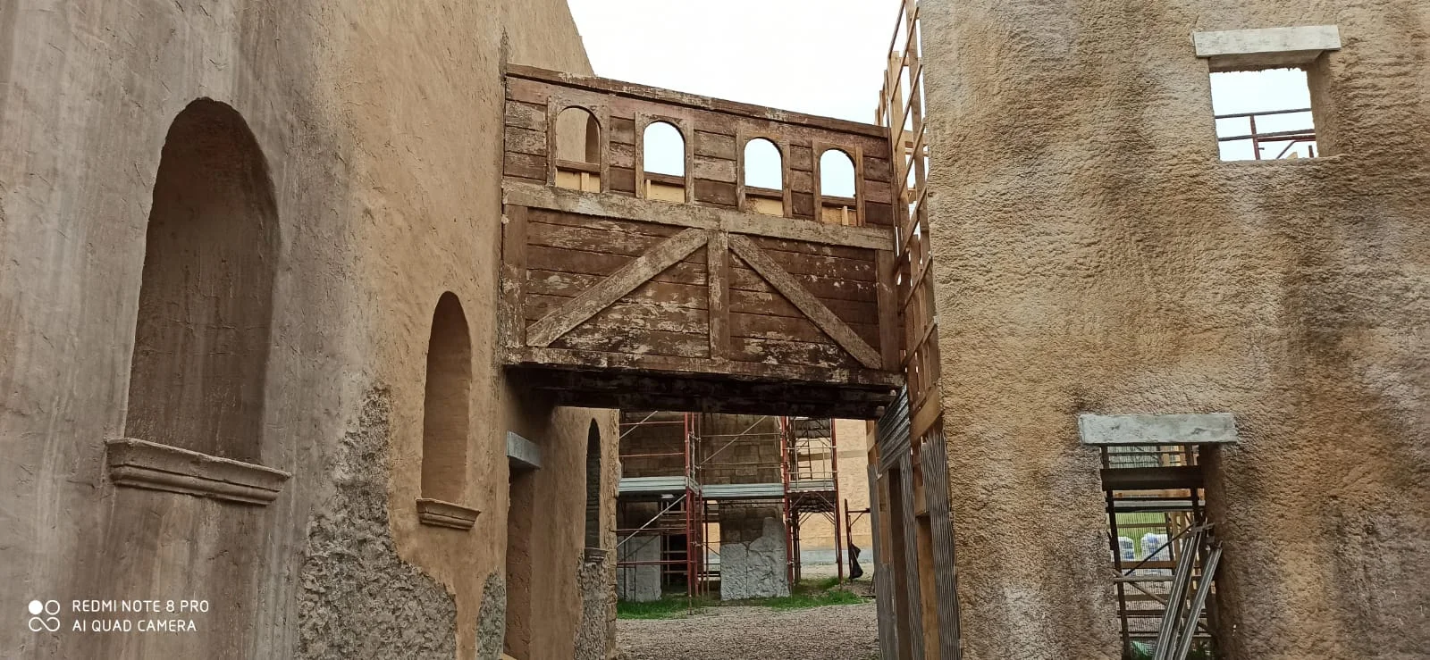 Ballatoio in legno sospeso sopra un passaggio fra due edifici del set: struttura in tavole di legno chiaro con balaustra a colonnine, archetti decorativi che incorniciano sei piccole bifore, sotto il ballatoio l'arco di passaggio fra le due ali del palazzo in finta pietra; ponteggi e attrezzatura del cantiere visibili sullo sfondo