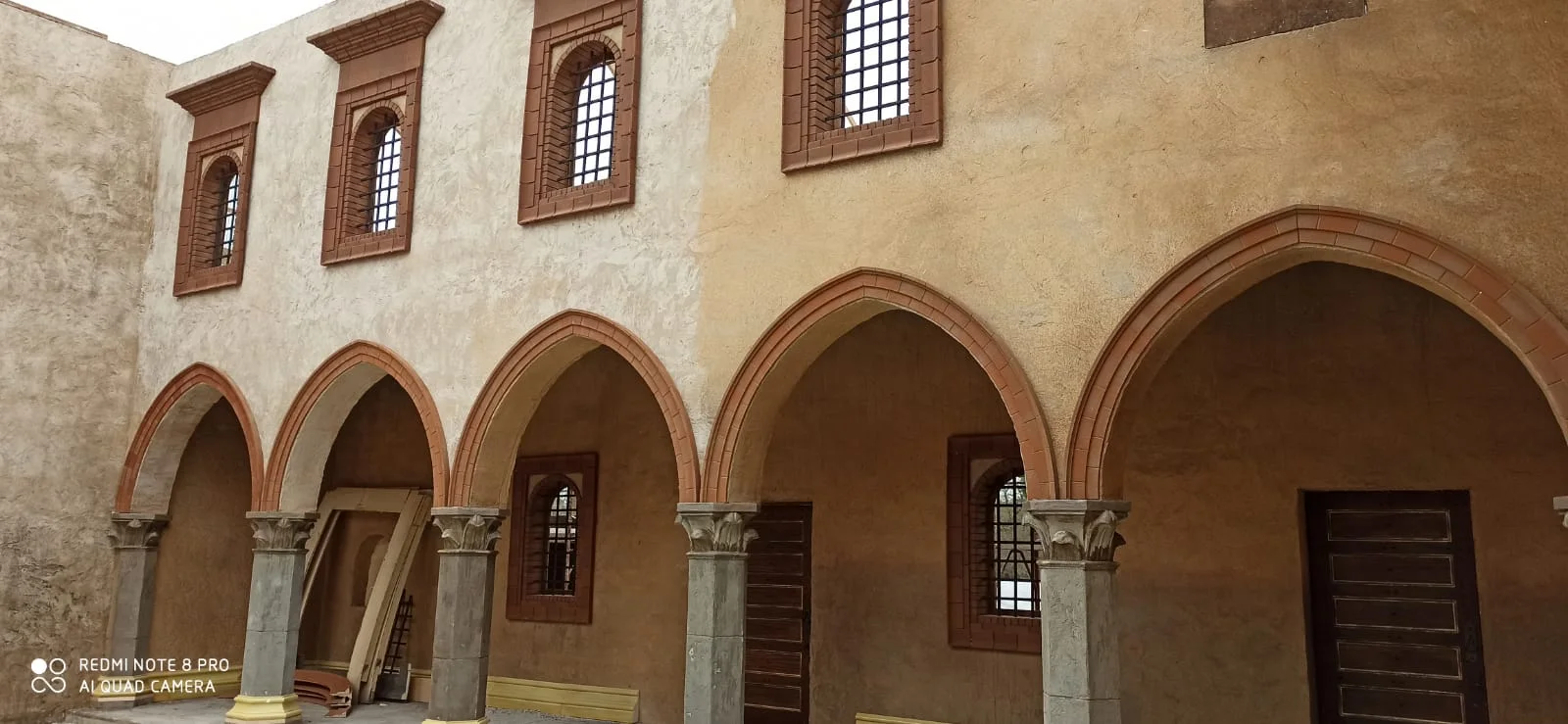 Cortile interno del palazzo lombardo: porticato a tre arcate ribassate con cornici in cotto rosso, colonne in pietra grigia con capitelli a foglie d'acanto, parete intonacata color sabbia-ocra, finestre bifore con cornici in cotto al piano superiore, tettuccio in travi di legno a vista