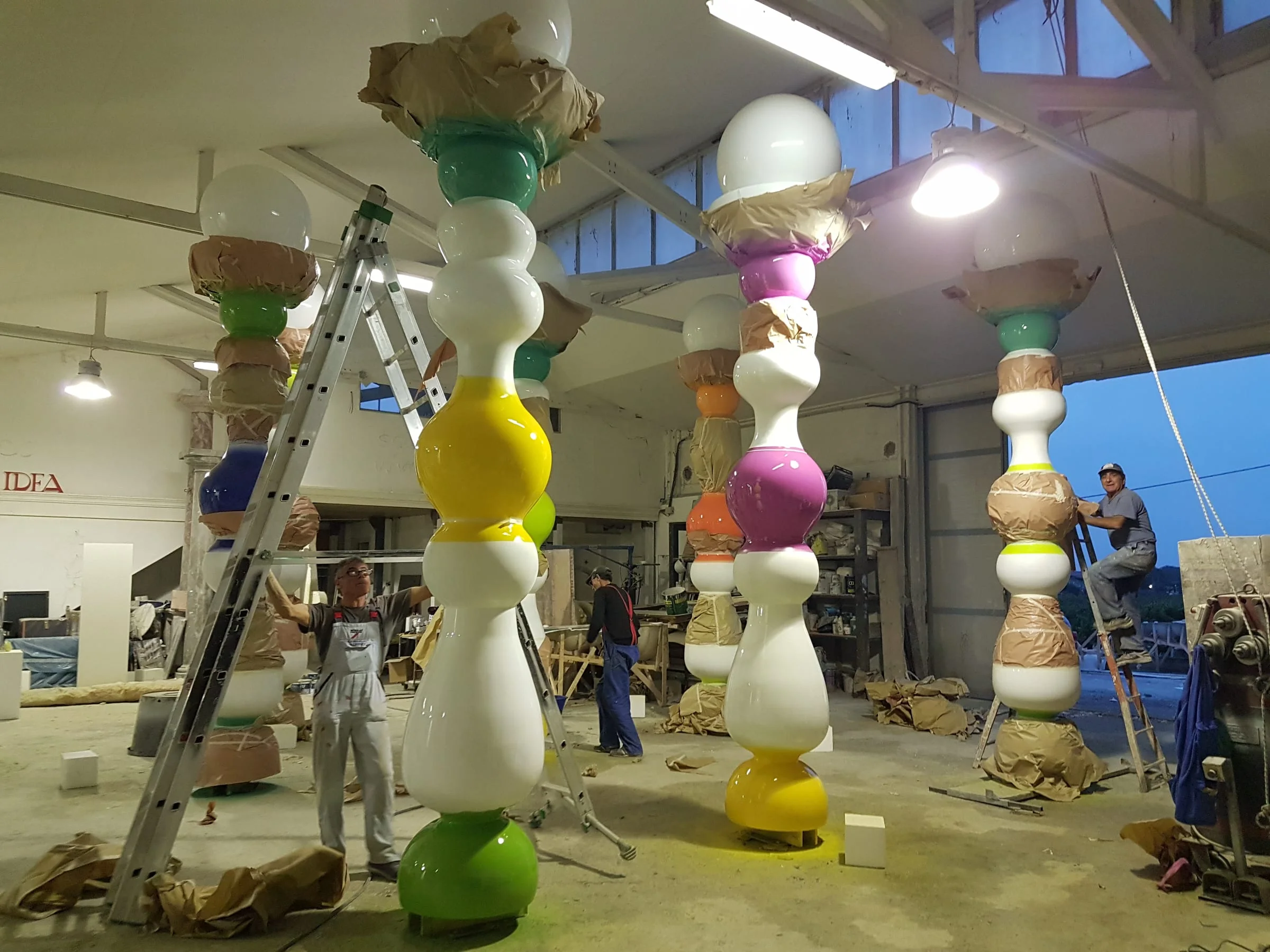 Finishing stage of the columns: raw pieces being sanded and prepared for painting, standing in the workshop yard