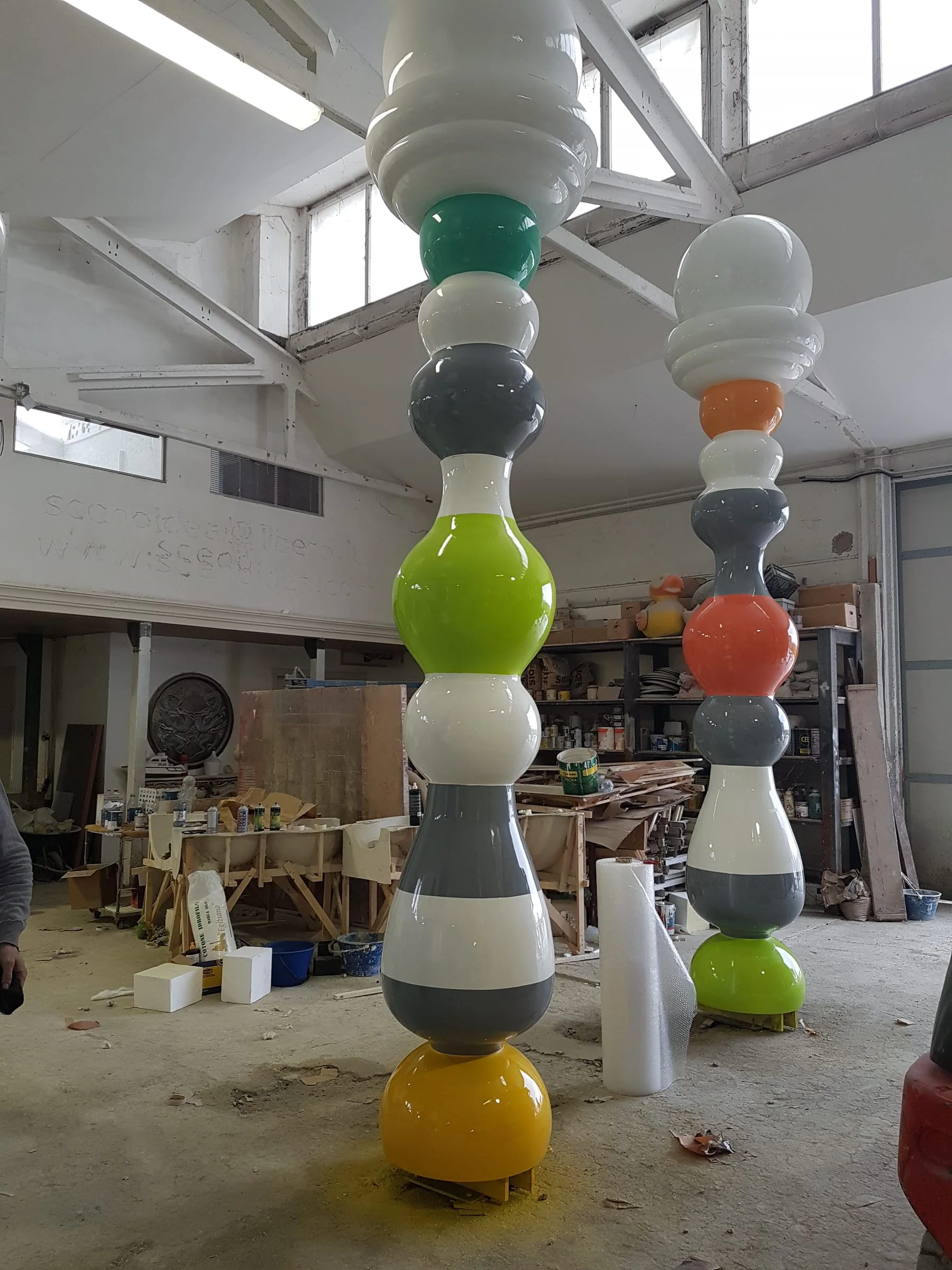 View of the painted columns in the workshop yard: polychrome pawns seen from a lateral angle, showing the balloon section and the broad base