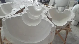 Open fiberglass moulds for making the columns: pawn-skittle-shaped shells in white porous material, mounted on wooden stands in the workshop, awaiting the fiberglass casting