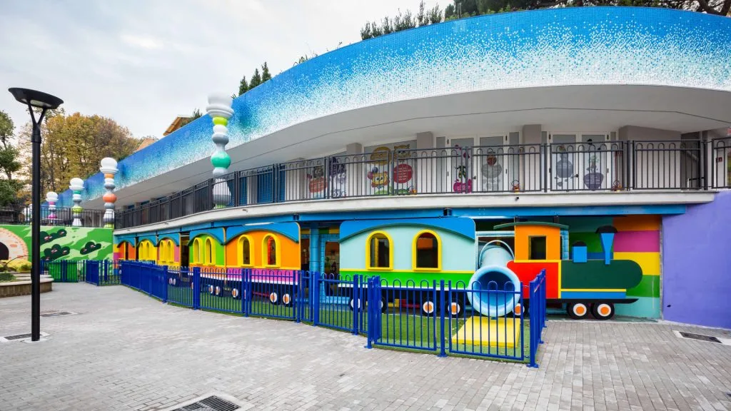 The Magicirco building at Luneur Park with blue mosaic roof and multicolour train on the ground floor: at the top-left, along the terrace edge, the seven pawn-columns made by Creation Art