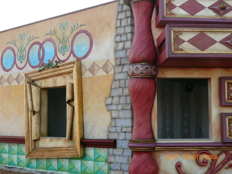 Detail of a fairy-tale facade: irregularly shaped golden stucco window frame, wall painted with turquoise circles, twisted red sculpted column, faux raw bricks
