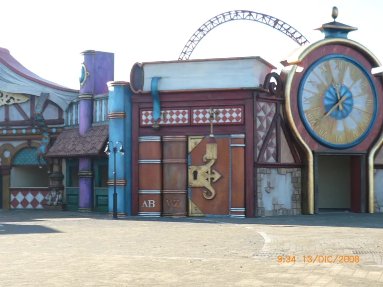 Portal of a 'books' theme park area: a large open book standing on the left functioning as a passage arch, a clock with a two-metre-tall Roman dial on the right, in the background the red-green structures of a roller coaster