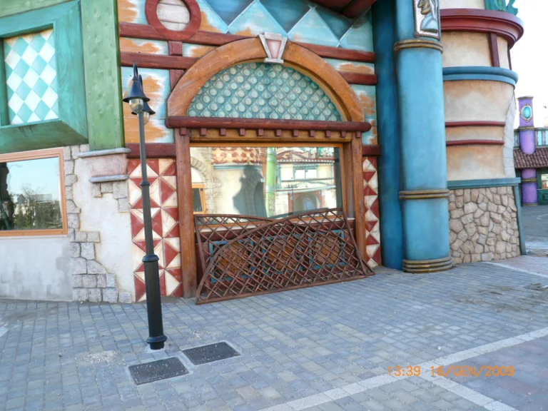 Park building portal: large arch with diamond geometric motif in aqua green and burgundy, twisted turquoise and red columns, oval window, black lamppost in the foreground