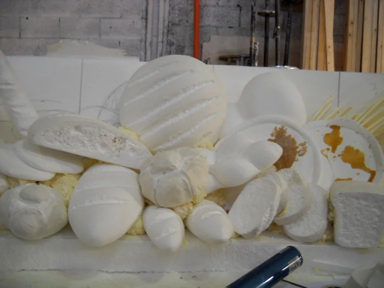 Workshop view of the bread counter in our studios: all the bread shapes carved in white expanded polystyrene before painting — striated round loaf, michette rolls, focaccia, biscuits, fougasse, oval rolls, on a yellowish polyurethane foam base