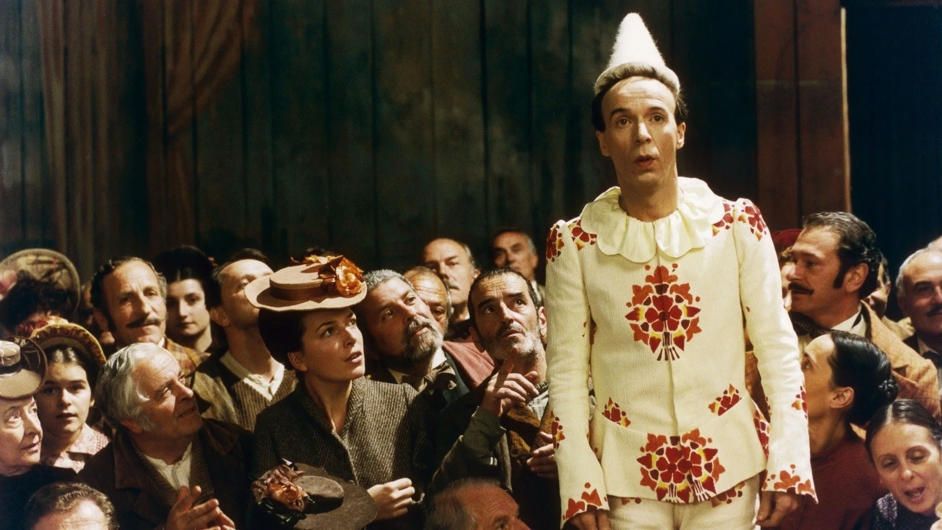 Pinocchio davanti al pubblico del teatro di Mangiafuoco — folla in costume ottocentesco, parete in legno lavorato del set.