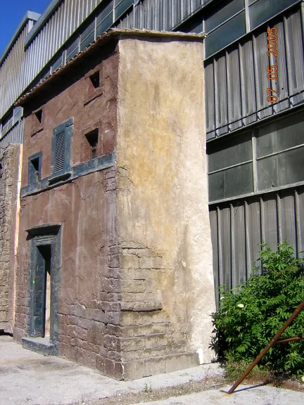 Edificio toscano a due piani con persiana dipinta, intonaco invecchiato a strappo e portale in pietra