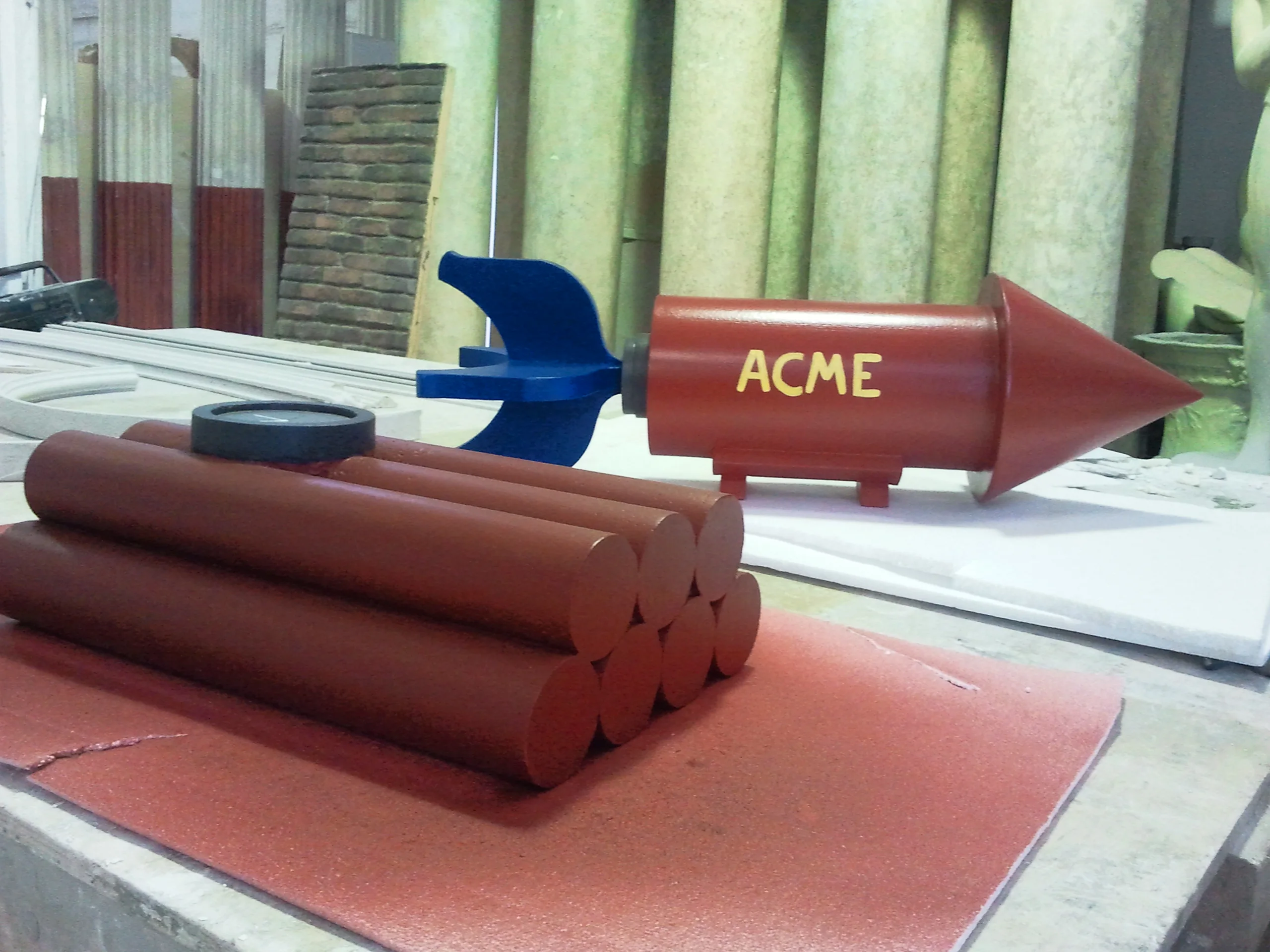 The finished set of ACME props, overall view in the workshop yard: on the right the ACME rocket bomb, in the foreground the dynamite with six cylinders, in the background classical column reproductions in storage and workshop equipment