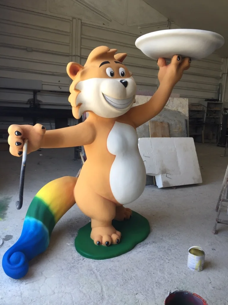 The monumental sculpture of the Gattobaleno, official mascot of Rainbow MagicLand, sculpted by Creation Art: magical cat in seated pose with rainbow livery, sculpted in full round in fibreglass, saturated polychrome finish in flat chromatic fields of the Rainbow Spa colour scheme, positioned in a visible area of the Valmontone park