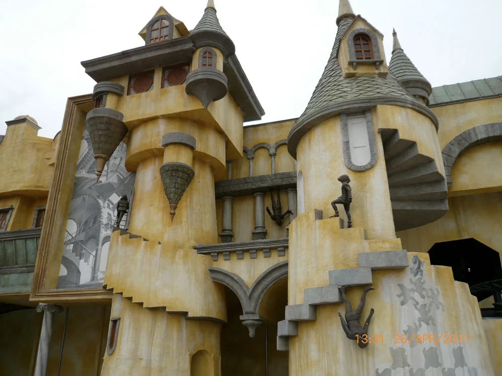 Maison Houdini on 26 April 2011: yellow Escher-style castle with green spired towers, inverted windows on the sides, painting of Escher's 'Relativity' lithograph on the side wall, sculpted bronze characters walking vertically on the walls