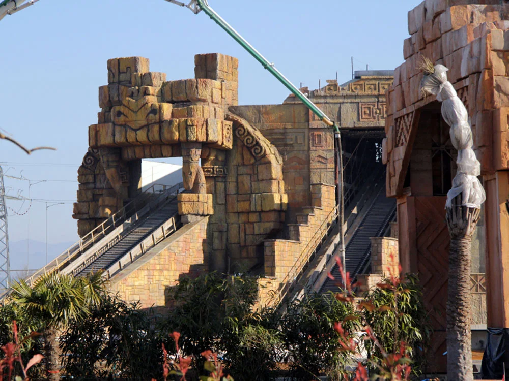 Yucatan in final construction phase: entrance gate of the pre-Columbian area with Mayan statues framing an attraction's slide, winter sky, load-bearing structure visible