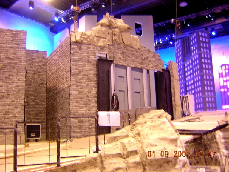 General three-quarter view of the construction: brick building with double grey door, profile of rocks on top, sculpted white cliff in the foreground, skyline of grey skyscrapers on the right of the studio with blue windows, dated 1 September 2005
