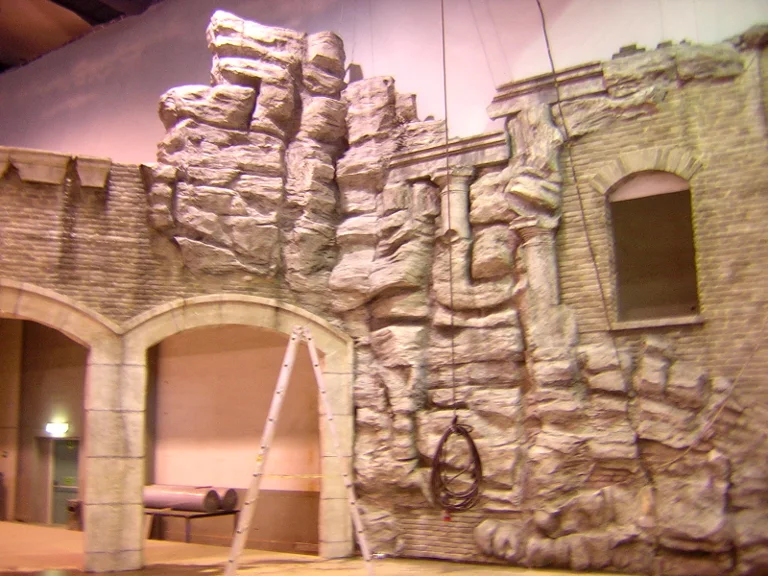 Detail of the ruin portal at the end of construction: faux stone arch on the left, brick wall turning into a vertical rocky cliff on the right, Corinthian stone columns, jagged windows, metal ladder in the centre
