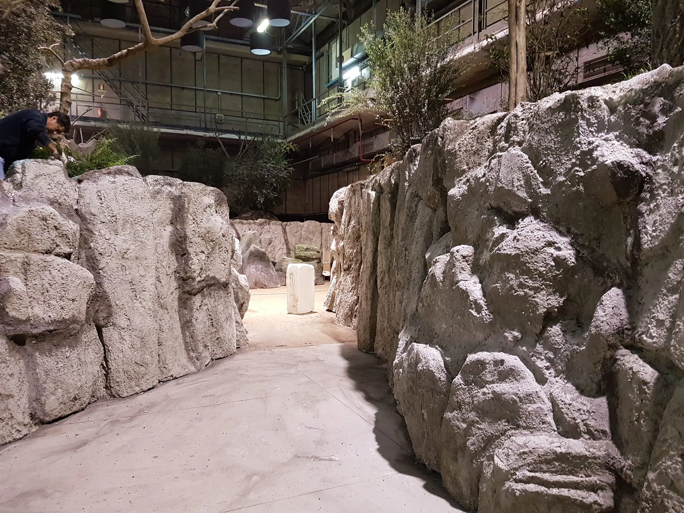 Indoor set of a rocky landscape: faux rock walls on either side of a passage, sculpted in angular volumes, lit from above by the studio walkways
