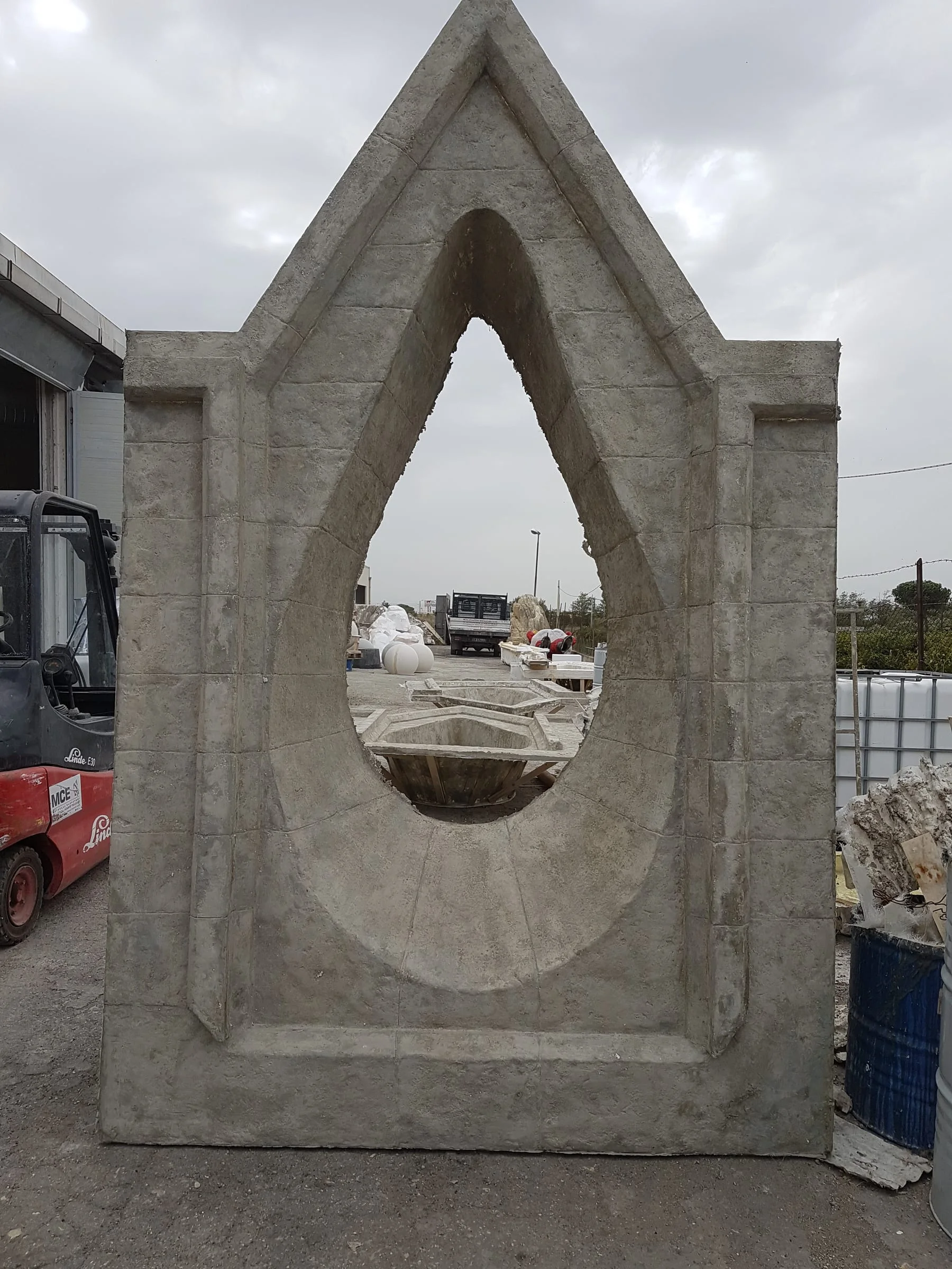 A large ogival portal finished in grey faux stone, about three metres tall, photographed in front of the shed with overcast sky. The vesica piscis shape is characteristic of Gothic architecture.