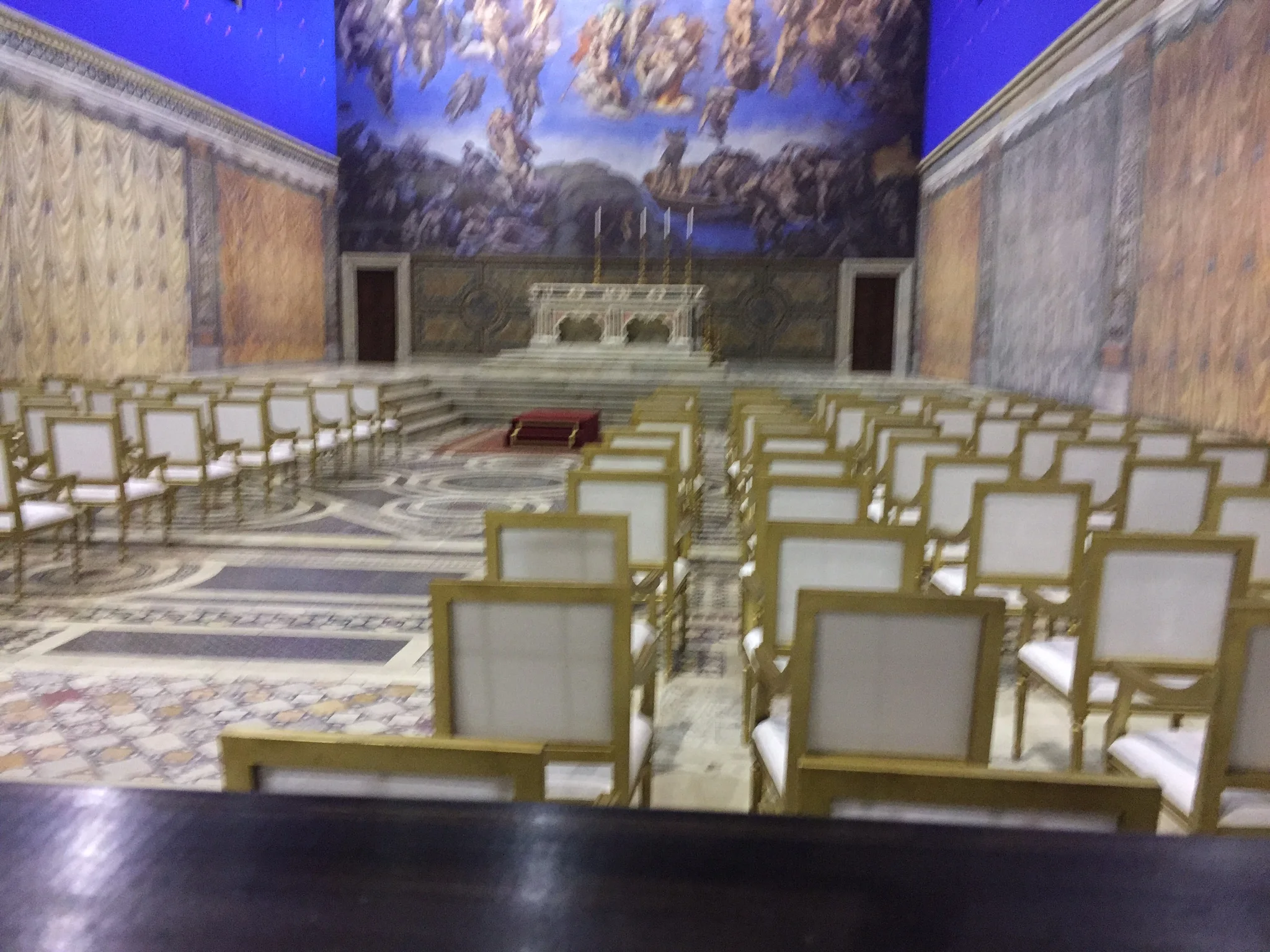 Altare papale al centro della cappella ricostruita: marmi finti, candelabri d'oro, sedie d'oro in file ordinate, fondale con affresco della Trasfigurazione sopra l'altare, cyclorama blu in alto