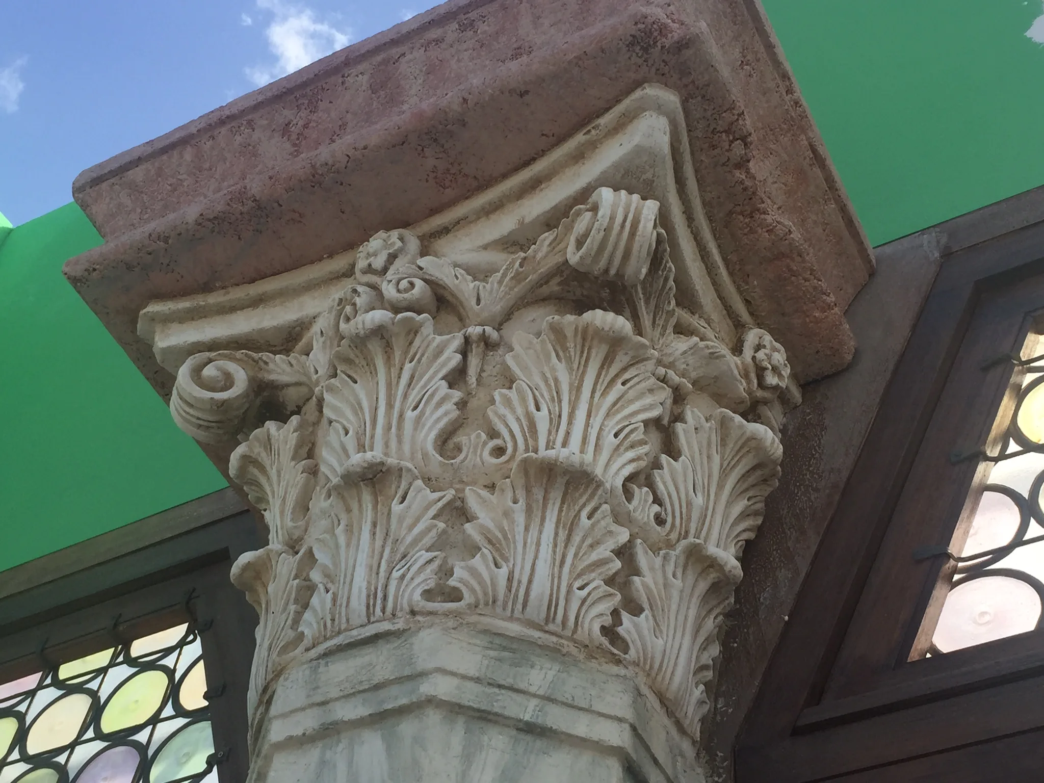 Dettaglio di un capitello corinzio in finto marmo scolpito: foglie d'acanto, volute angolari, dado sopra, perfettamente classico ma con cromaticità da set