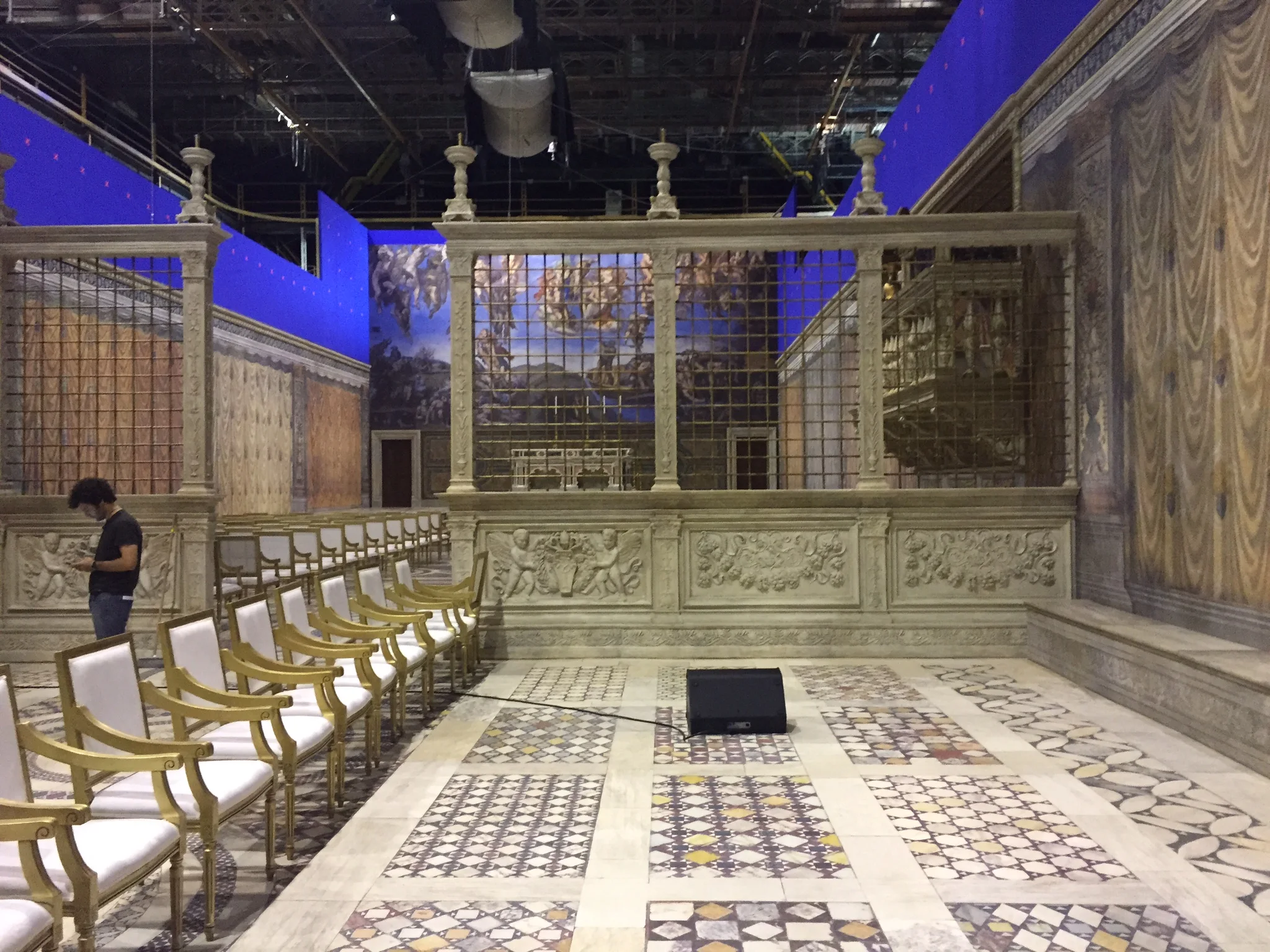 Vista del set della cappella papale ricostruita al Teatro 5 di Cinecittà: pavimentazione cosmatesca a mosaico, sedie d'oro in file, balaustra scolpita, riproduzione del Giudizio Universale michelangiolesco alle pareti, cyclorama blu sullo sfondo.