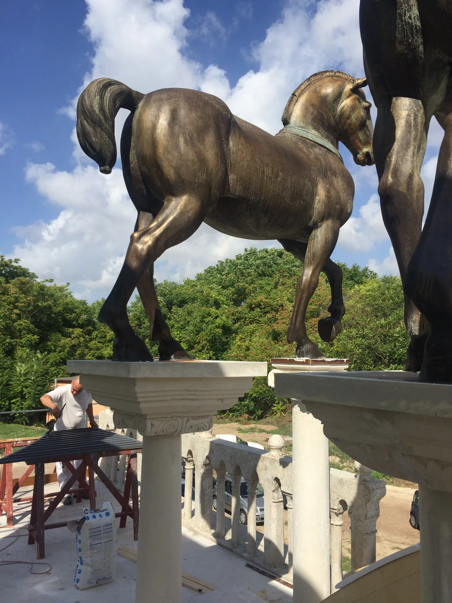 Vista 3/4 di una quadriga finita sul set con chroma key blu di sfondo, balaustra in finto marmo bianco con bassorilievi sotto, una persona vicino in lavorazione